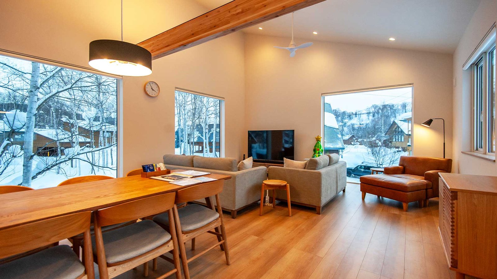 “Bright open-plan living and dining area at Wakoto Chalet, The Country Resort Niseko, with large windows overlooking the snowy forest.”