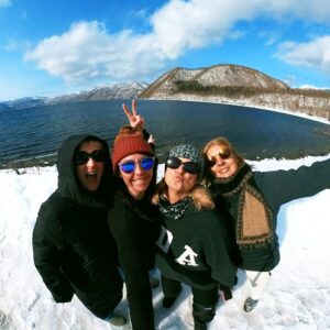 Four women from Women on Edge ski retreat smiling at Lake Shiribetsu, Hokkaido — enjoying a day of adventure and connection off the slopes.